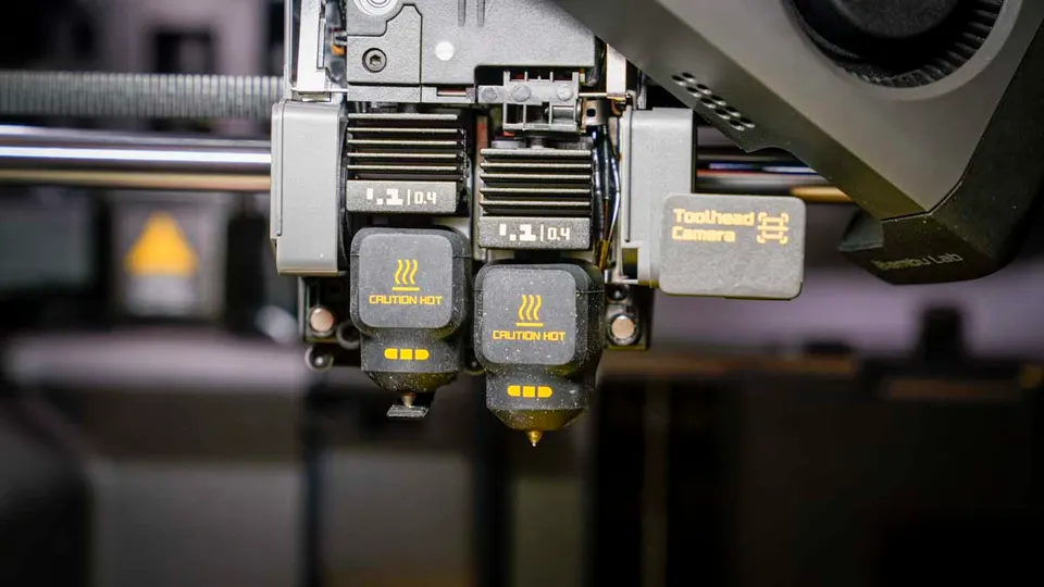 Detail dvou samostatných trysek na tiskové hlavě 3D tiskárny Bambu Lab.