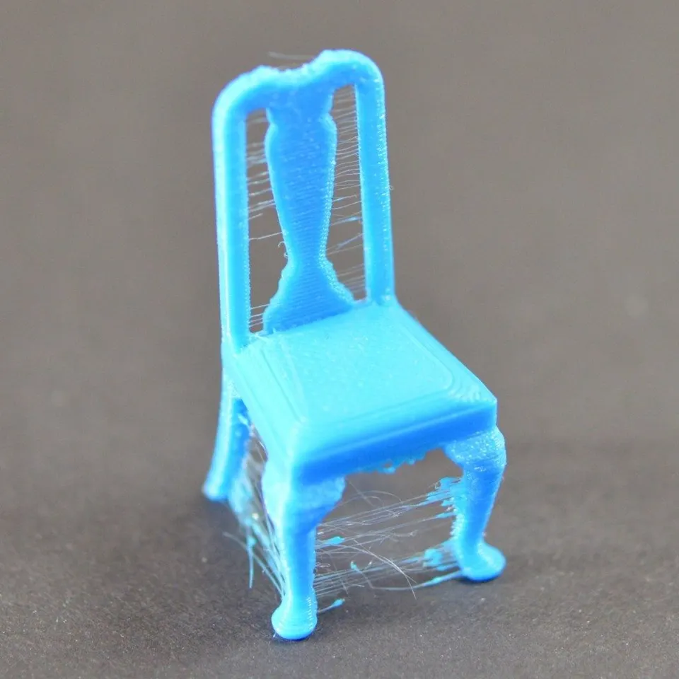 Modrý 3D tištěný model židle s tenkými plastovými chloupky mezi částmi výtisku.