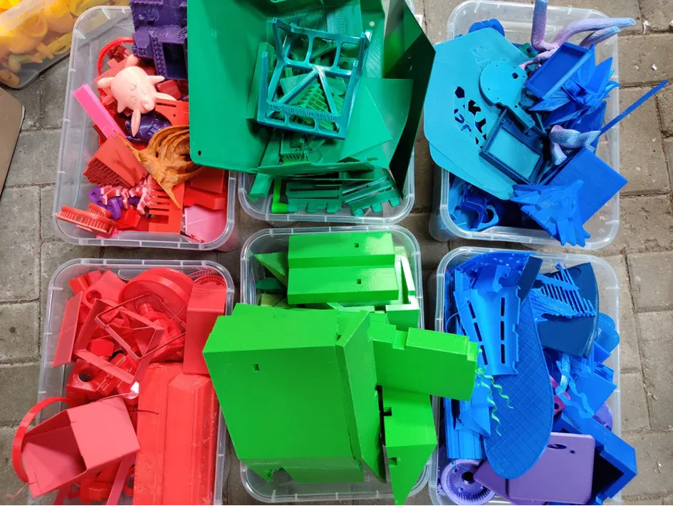 Zbytky z 3D tisku roztříděné do samostatných plastových nádob podle barvy a materiálu.